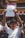 A person is holding up a document with multiple signatures and a stamp, standing among a crowd of people. The individual is dressed in a white shirt and wearing a black headband. The background shows part of a building with red and white banners.