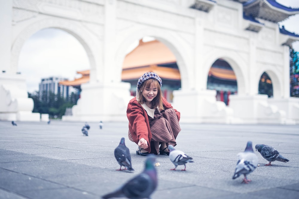 woman in red jacket sitting on sidewalk during daytime