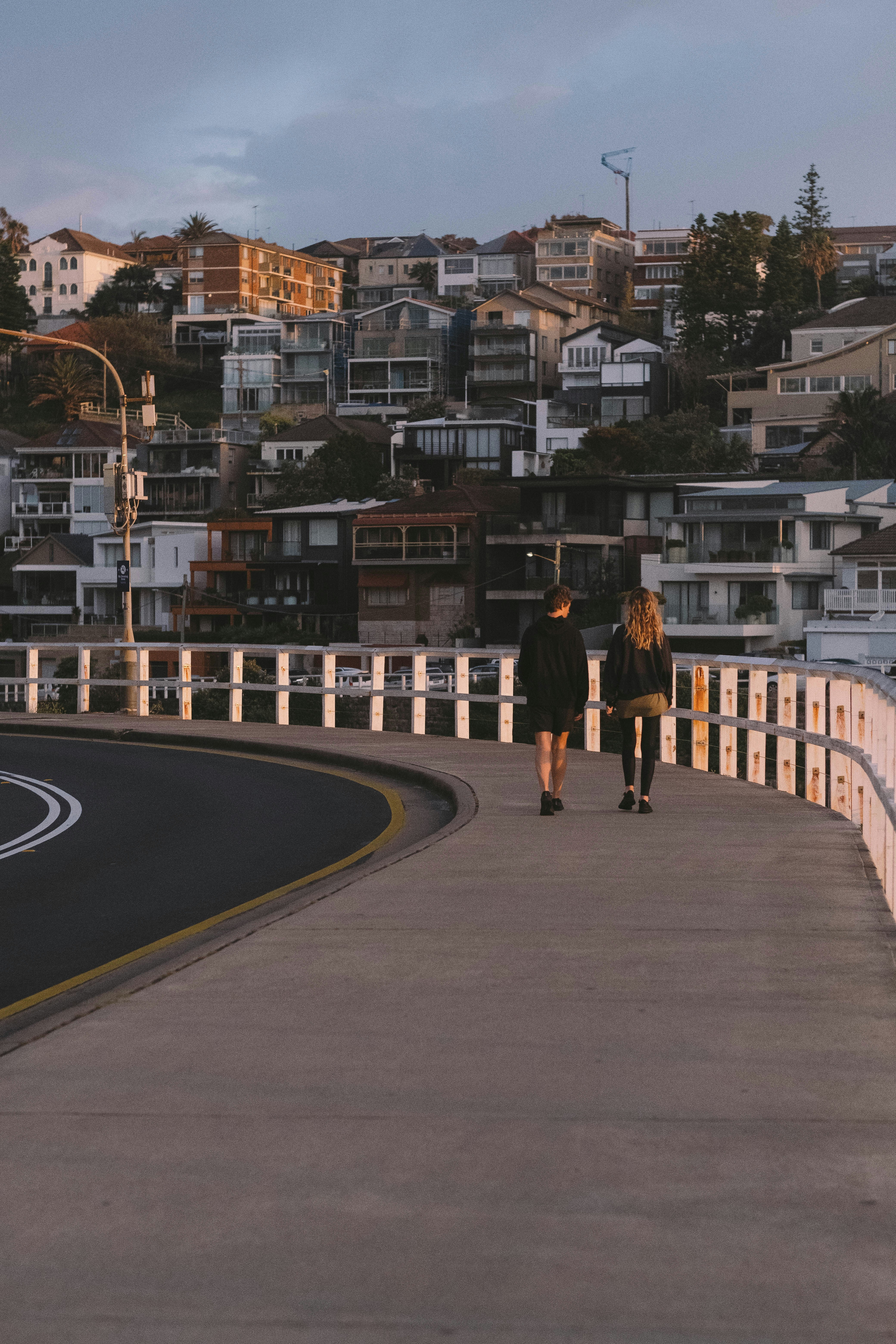 Hombre con chaqueta negra y pantalones negros caminando por la carretera de asfalto gris durante el día