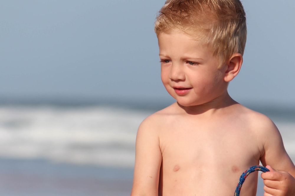 topless boy standing on beach during daytime