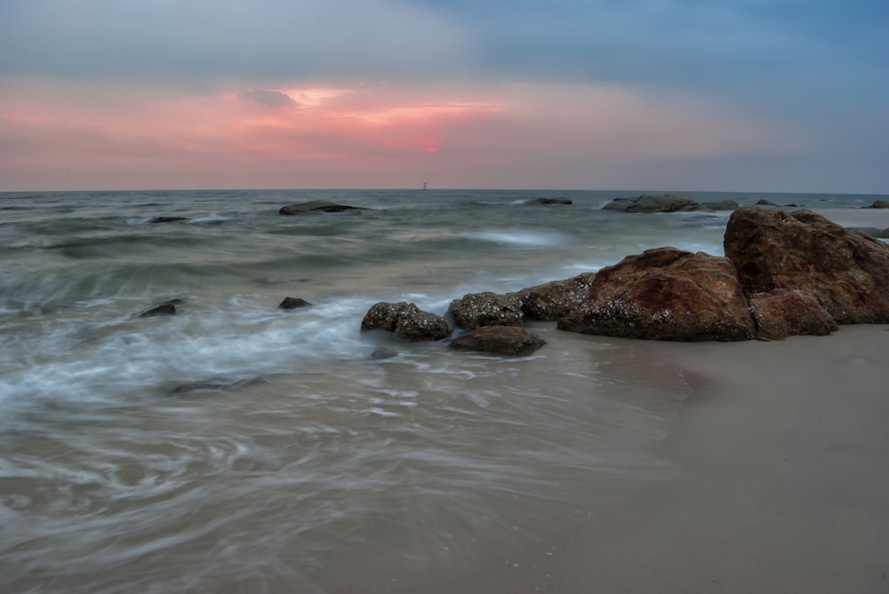 brown rock formation on sea water during sunset