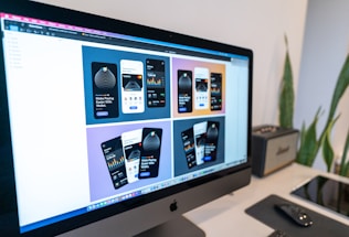 A computer monitor displaying a design mock-up for a mobile payment application. The screen shows six design variations with different color schemes and layouts. A desk setup is visible in the background, including a keyboard, mouse, graphics tablet, and some plants.