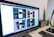 A computer monitor displaying a design mock-up for a mobile payment application. The screen shows six design variations with different color schemes and layouts. A desk setup is visible in the background, including a keyboard, mouse, graphics tablet, and some plants.