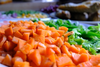 Brightly colored diced carrots and green bell peppers are prominently displayed, with other blurred vegetables in the background suggesting a preparation for cooking.
