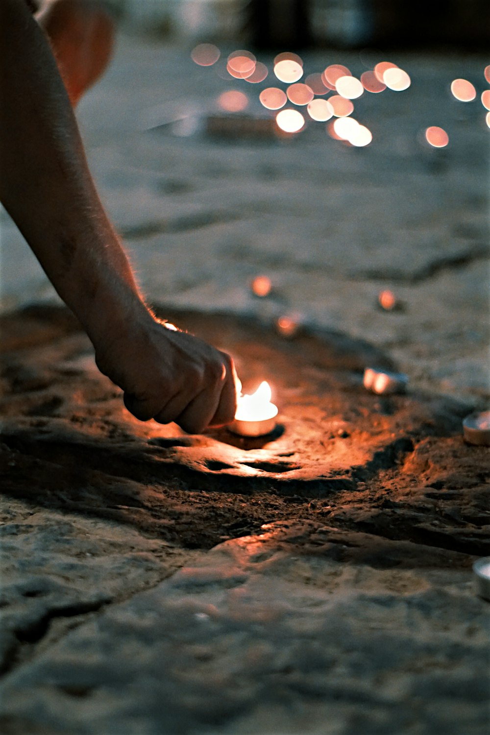 person holding lighted candle on brown sand during night time