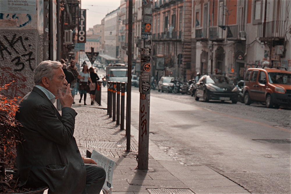 man in black jacket sitting on bench near road during daytime