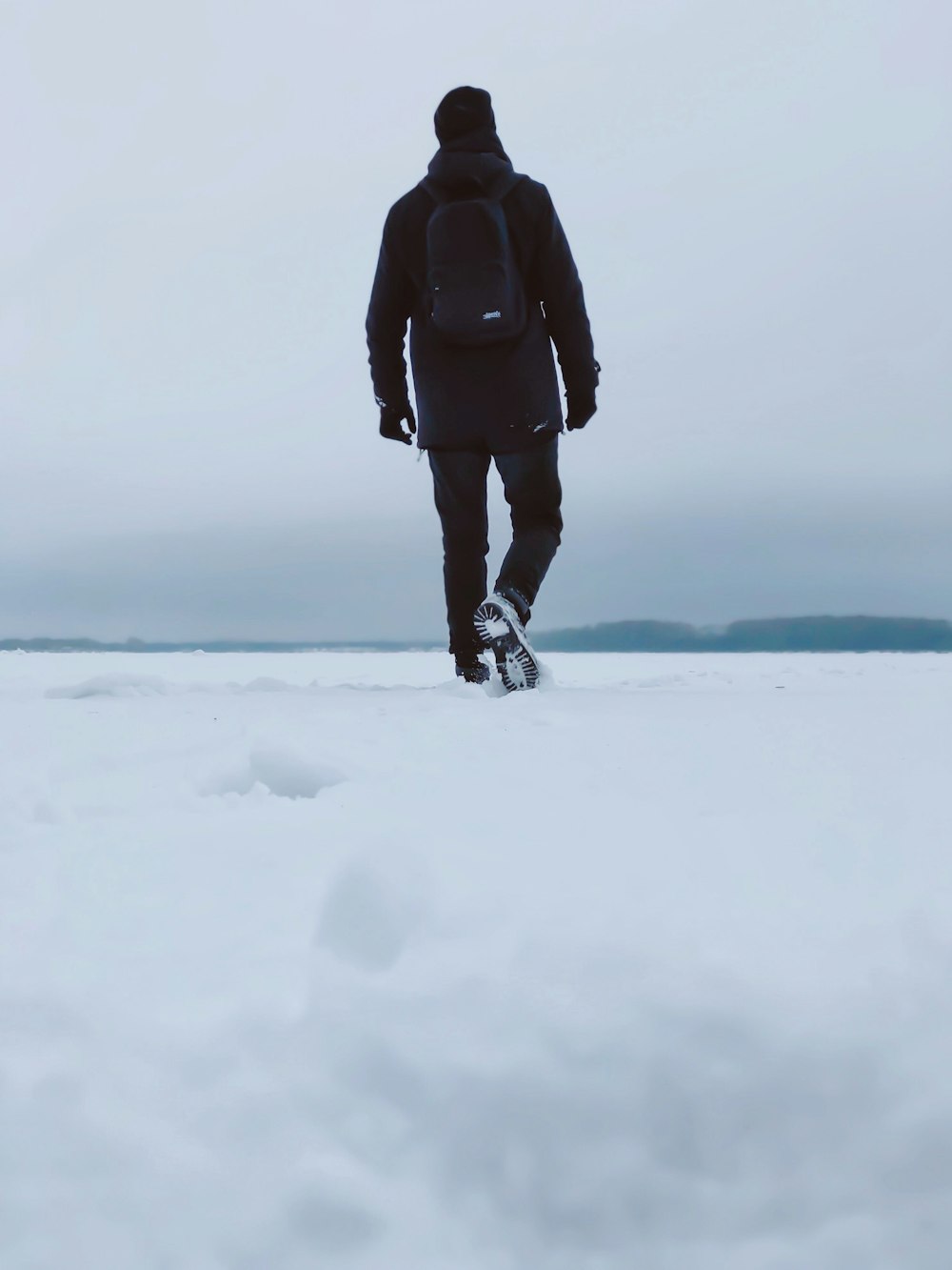 Persona con chaqueta negra y pantalones negros de pie en suelo cubierto de nieve