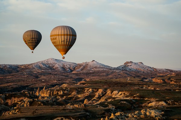 Two balloons drifting above Cappadocia's volcanic landscape