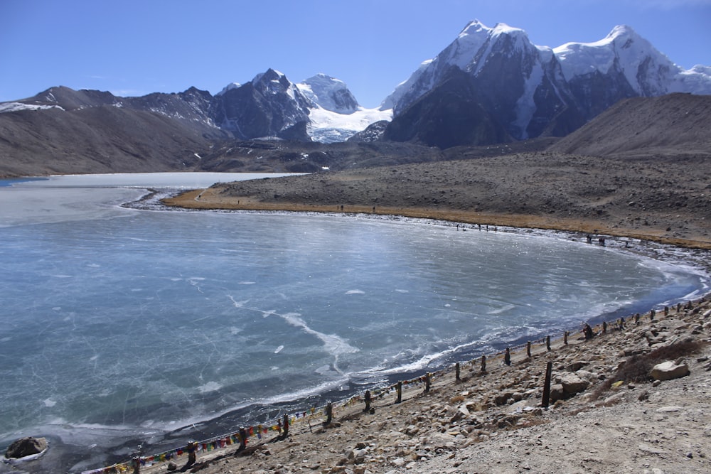 brown wooden fence near body of water and mountain during daytime