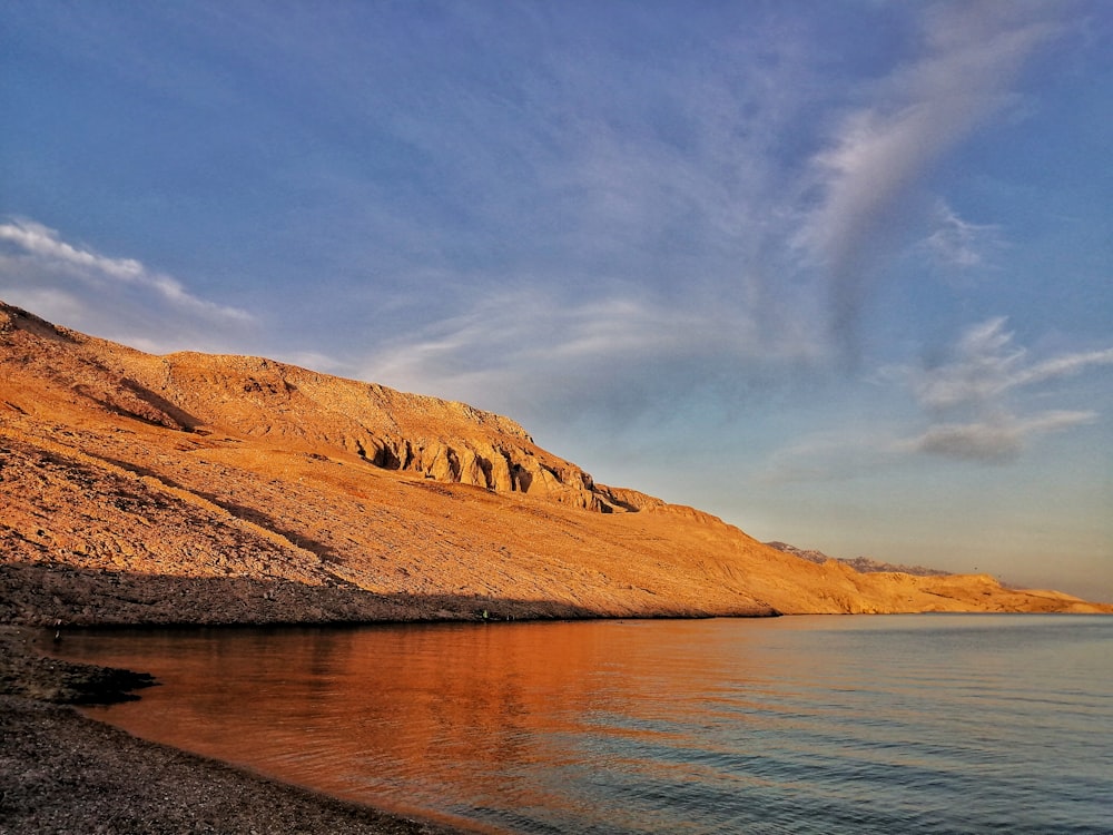 brown mountain beside body of water under blue sky during daytime