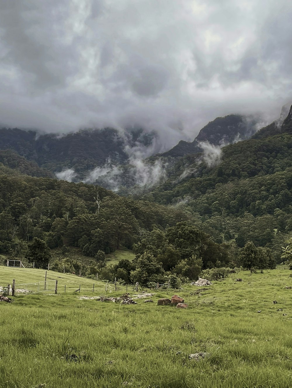 green grass field near green mountain under white clouds during daytime