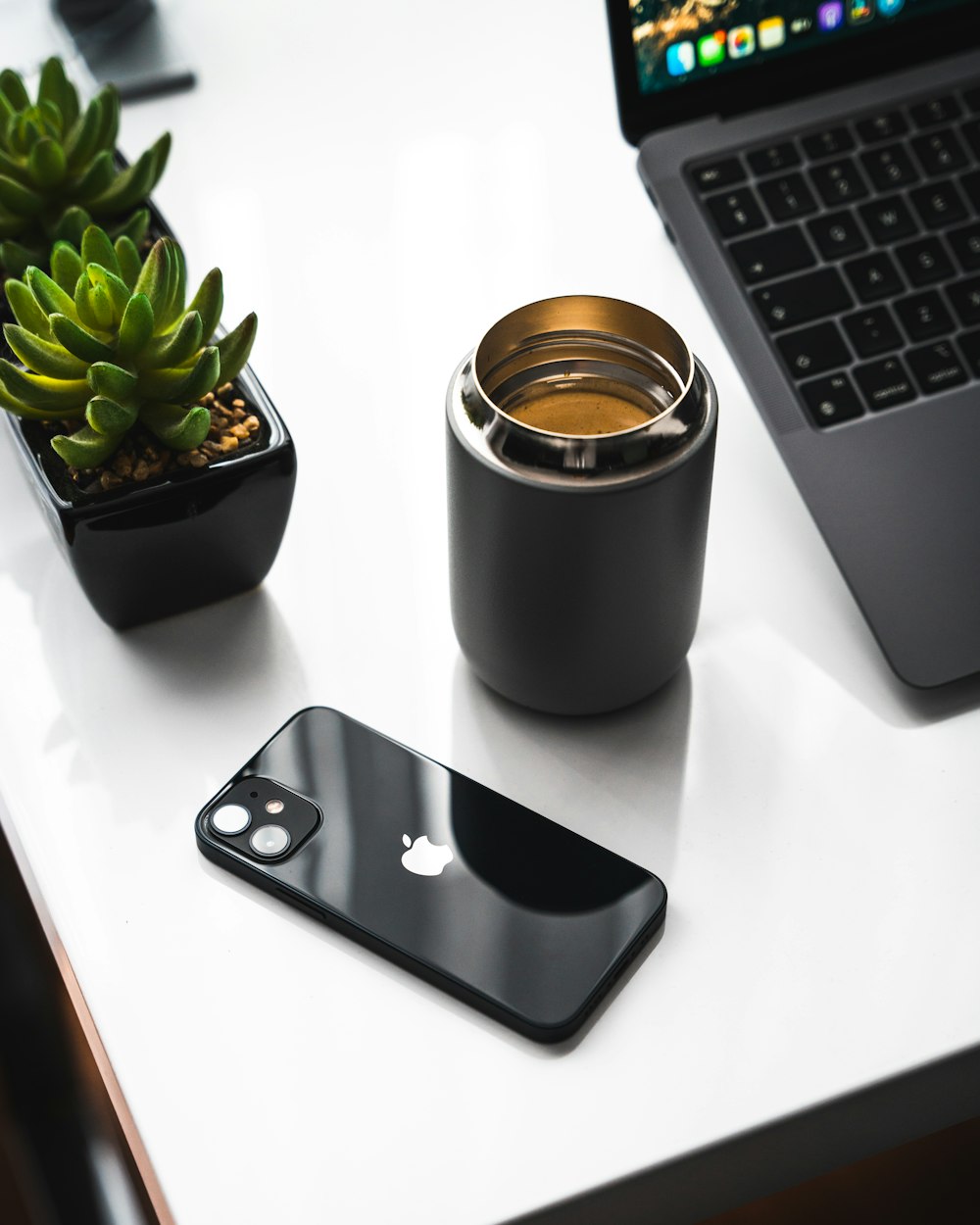 iPhone 6 plateado junto a taza de cerámica negra sobre mesa blanca