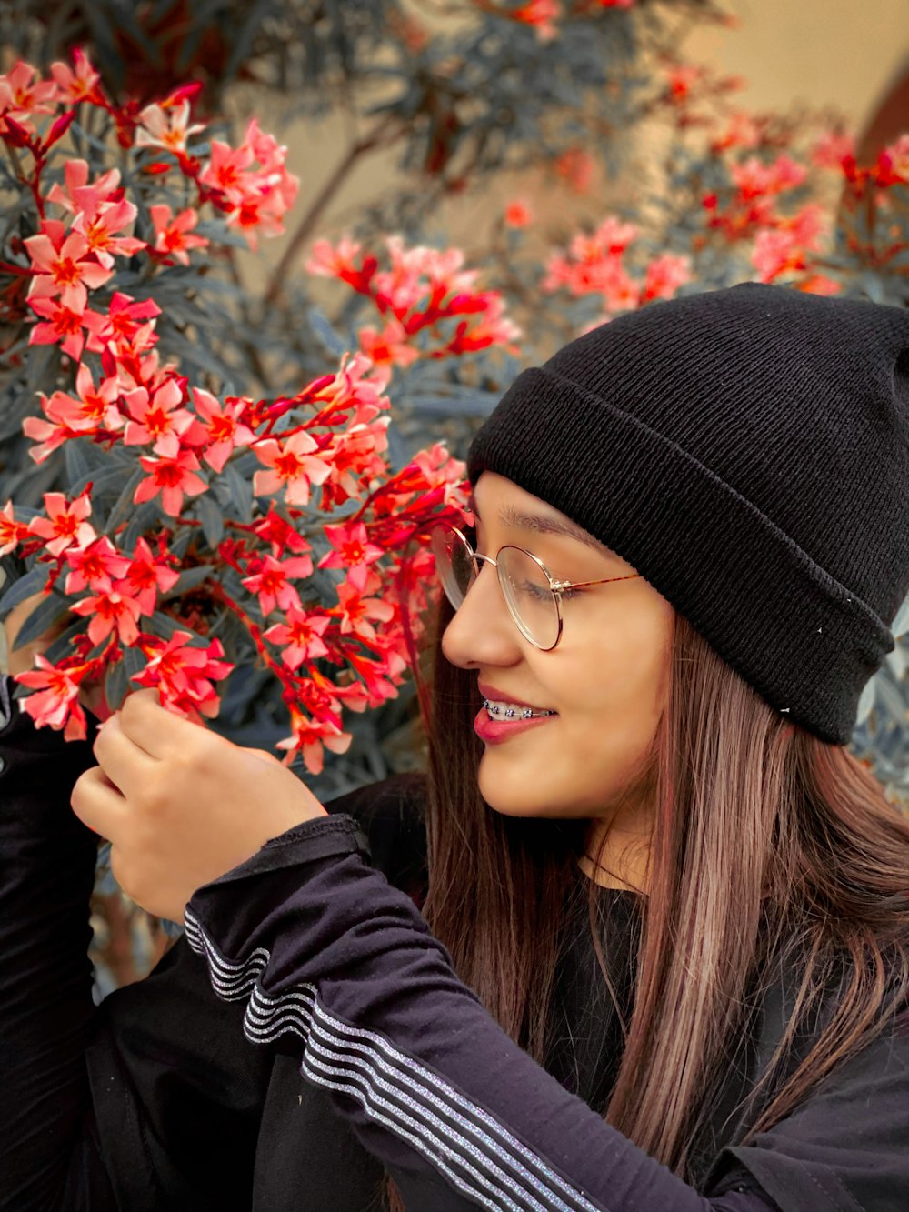 woman in black knit cap and black framed eyeglasses holding red flowers
