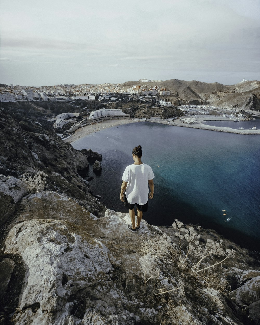 man in white long sleeve shirt and black shorts standing on rocky mountain looking at blue