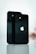 Two black smartphones are standing upright on a reflective surface. The Apple logo is prominently displayed on both devices. The background is softly blurred, emphasizing the sleek design and the glossy finish of the phones.