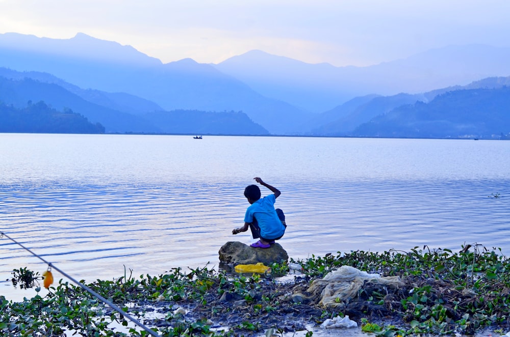 Mujer en camisa azul sentada en la roca junto al mar durante el día