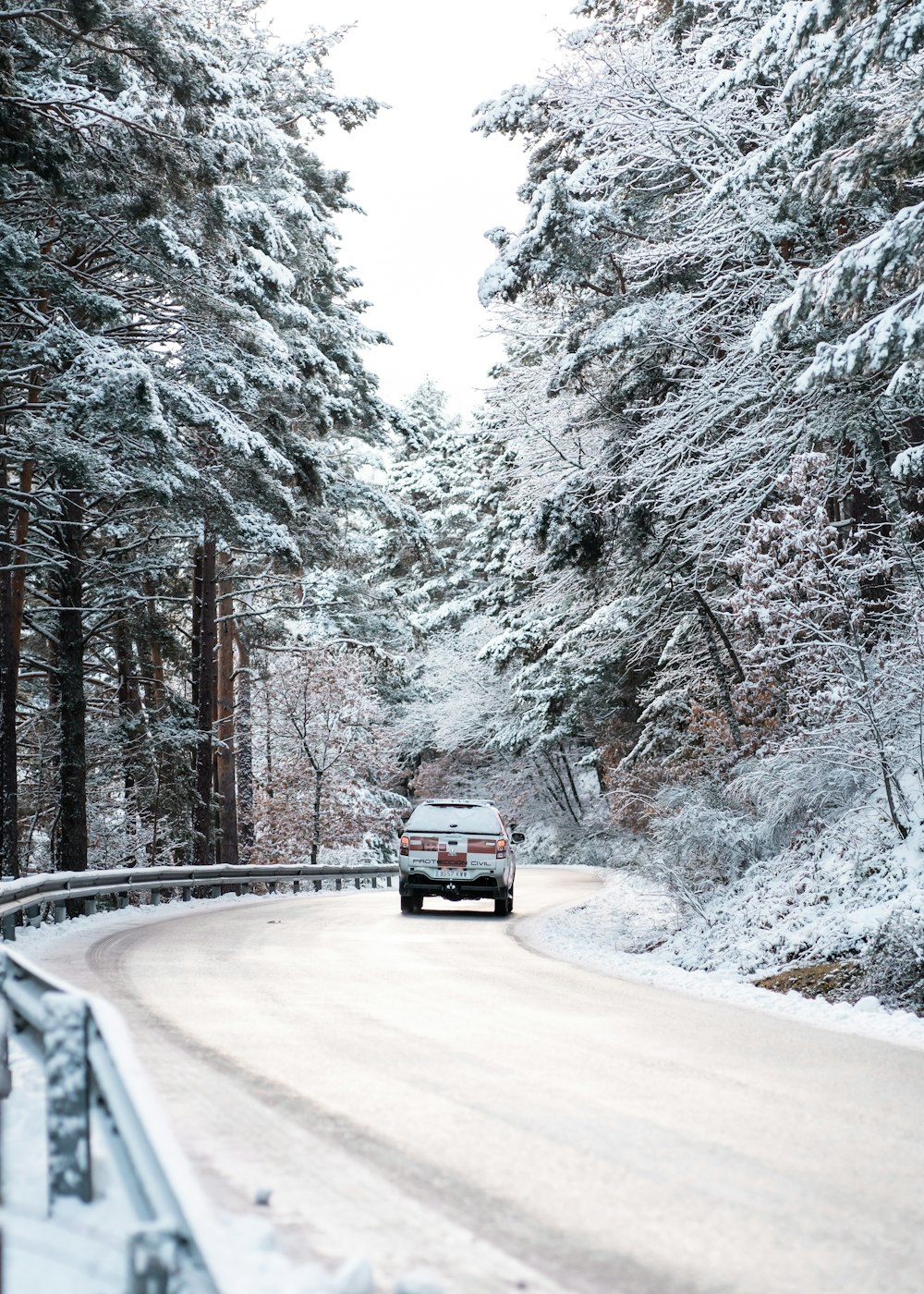 white suv on road between trees covered with snow during daytime