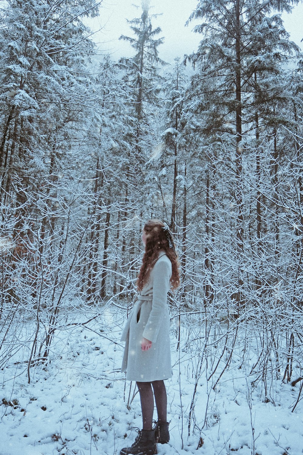 woman in white dress standing on snow covered ground surrounded by trees during daytime