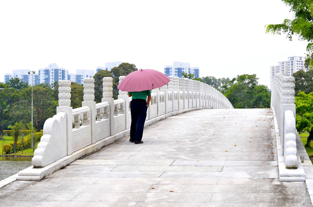 검은 바지를 입은 여자��가 분홍색 우산을 들고 낮에 보도를 걷고 있다