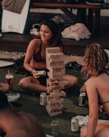 A group of friends joyfully playing giant Jenga on a sunny backyard lawn.