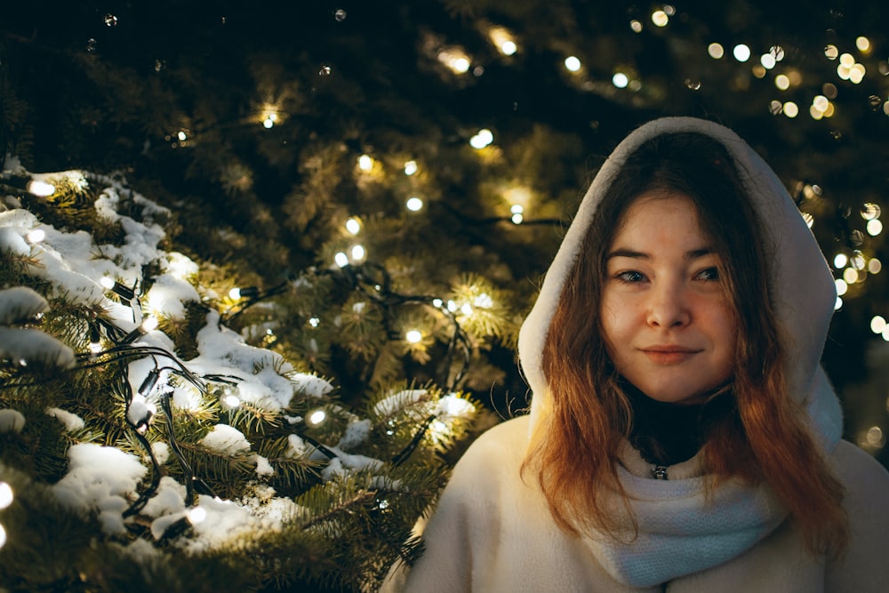 woman in white turtleneck shirt standing beside green christmas tree with string lights