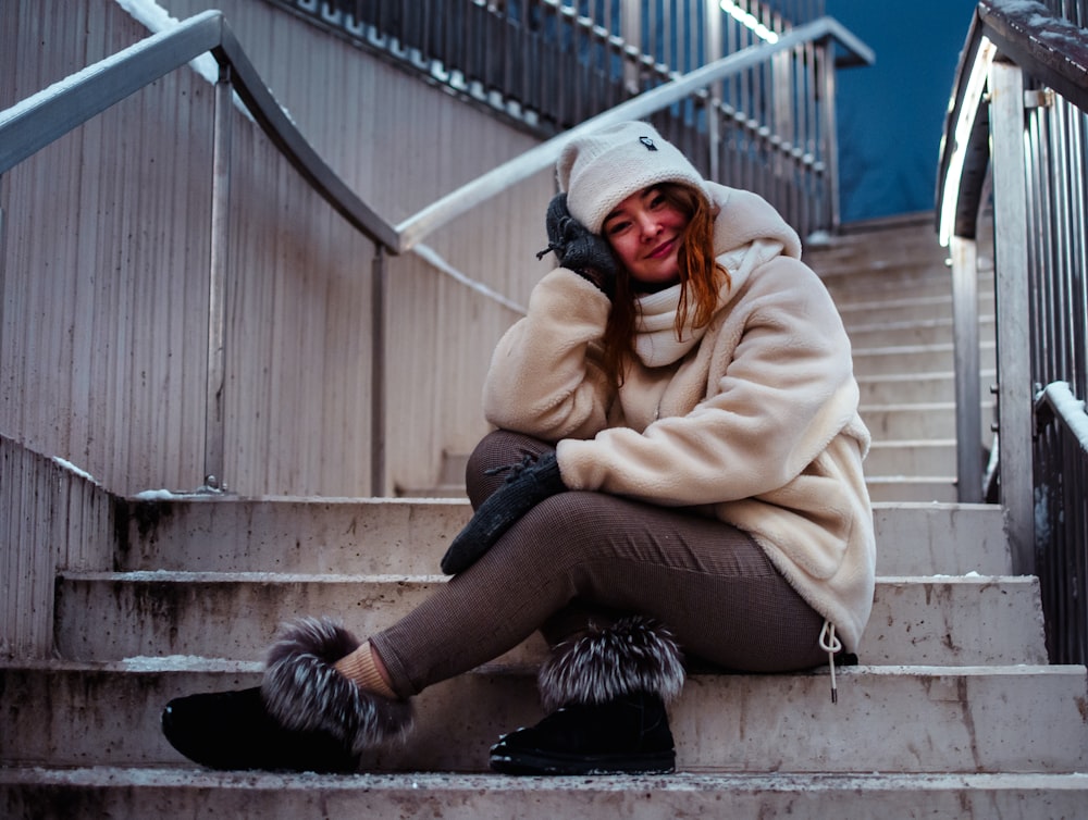 woman in beige coat and black pants sitting on stairs