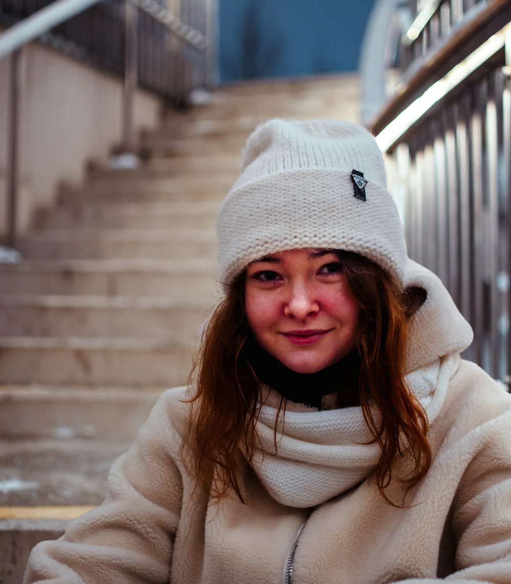 girl in white knit cap and white coat standing on gray concrete stairs during daytime