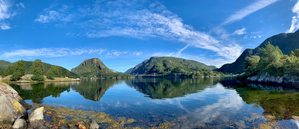 montanha verde e marrom ao lado do lago sob o céu azul e nuvens brancas durante o dia