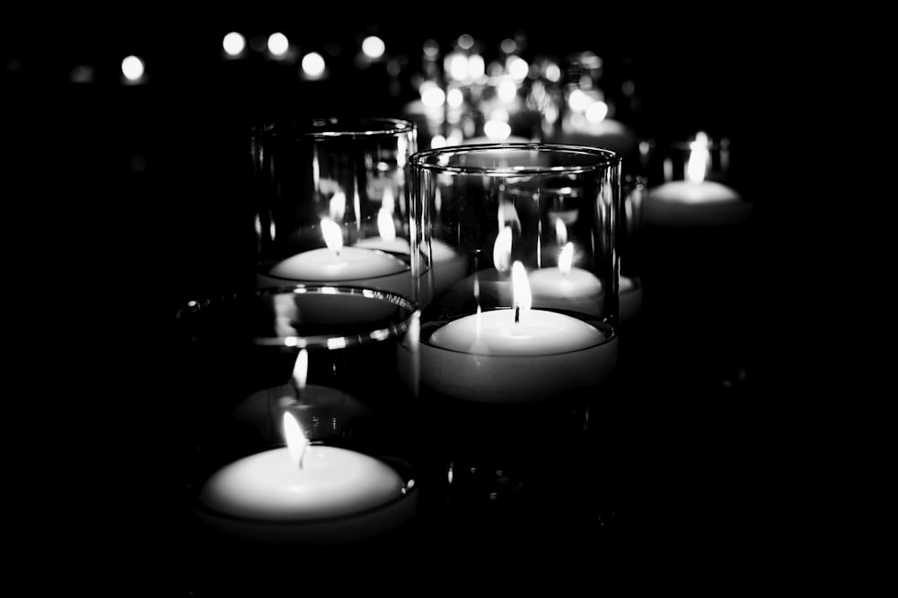 grayscale photo of candles on glass containers