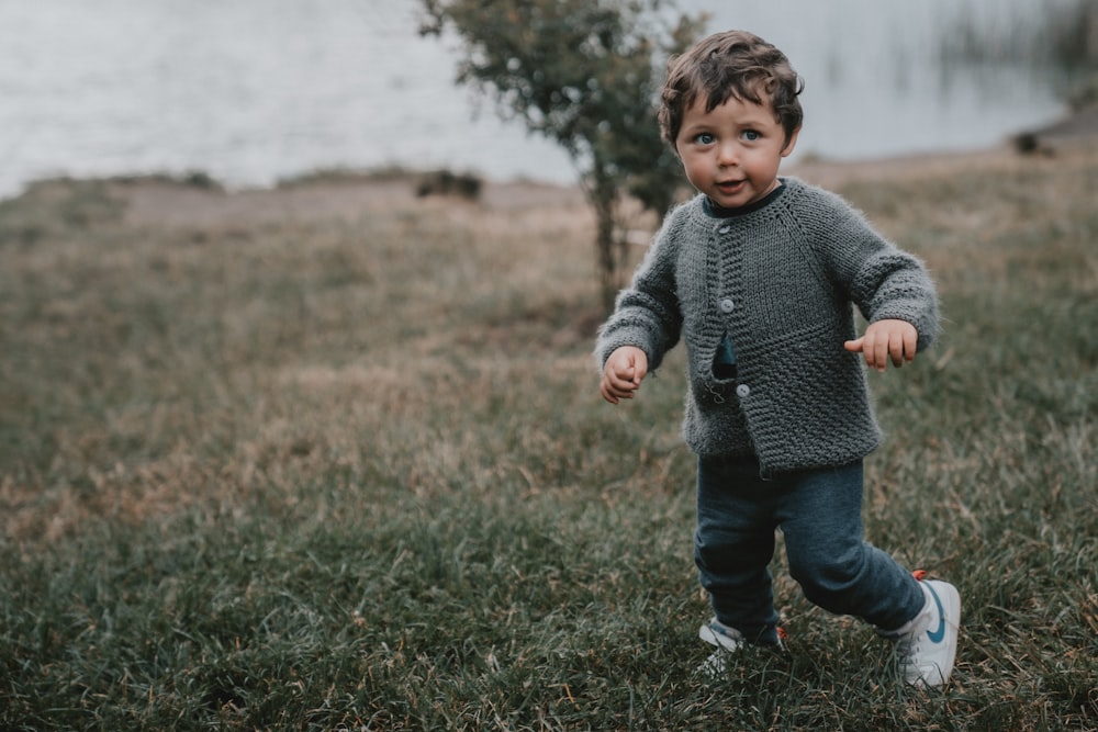 boy in gray sweater and blue denim jeans standing on green grass field during daytime