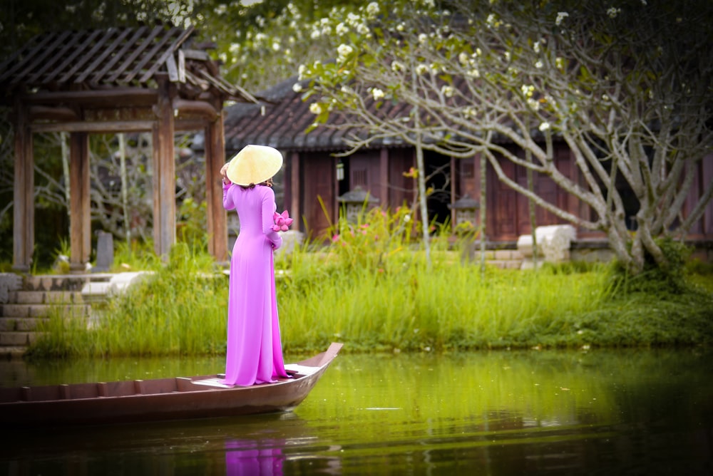 낮 동안 호수에 갈색 나무 보트에 분홍색 드레스를 입은 여자