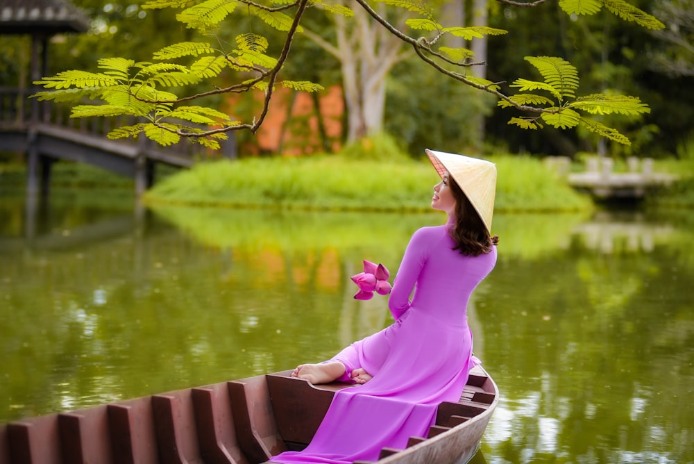 woman in pink long sleeve shirt sitting on brown wooden boat on lake during daytime