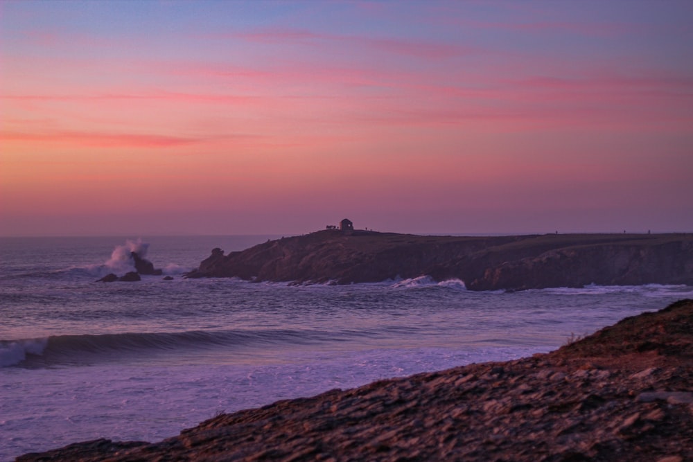 pessoa em pé na formação rochosa perto do mar durante o pôr do sol