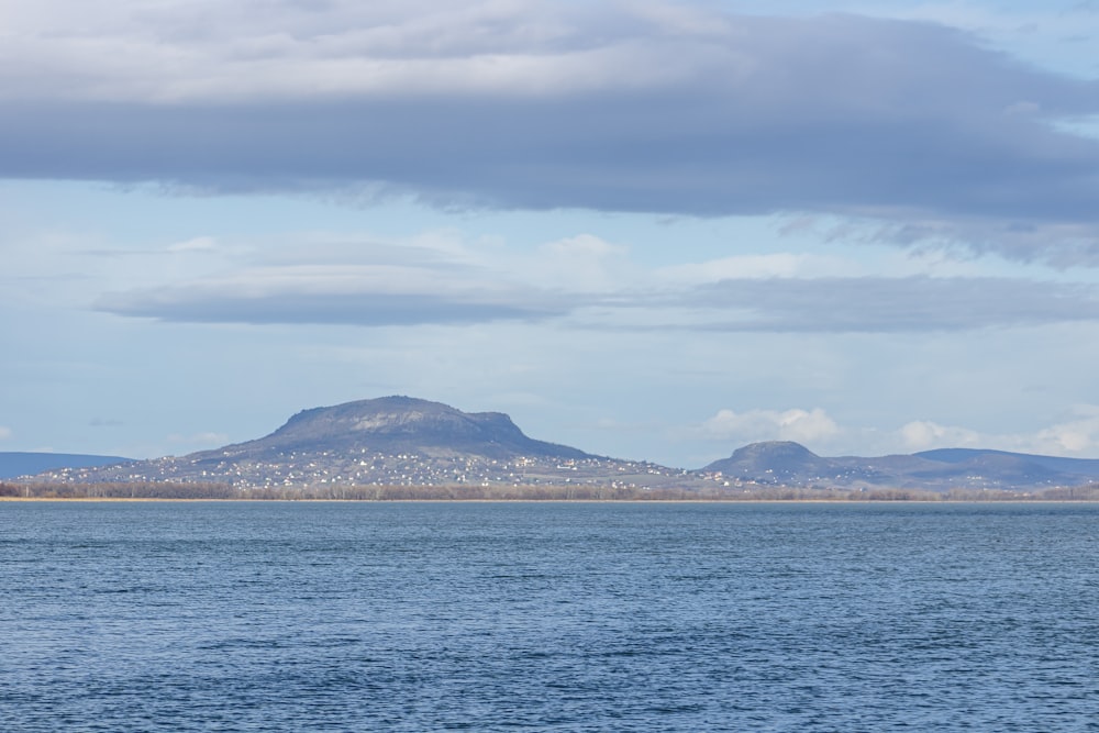 body of water near mountain under white clouds during daytime