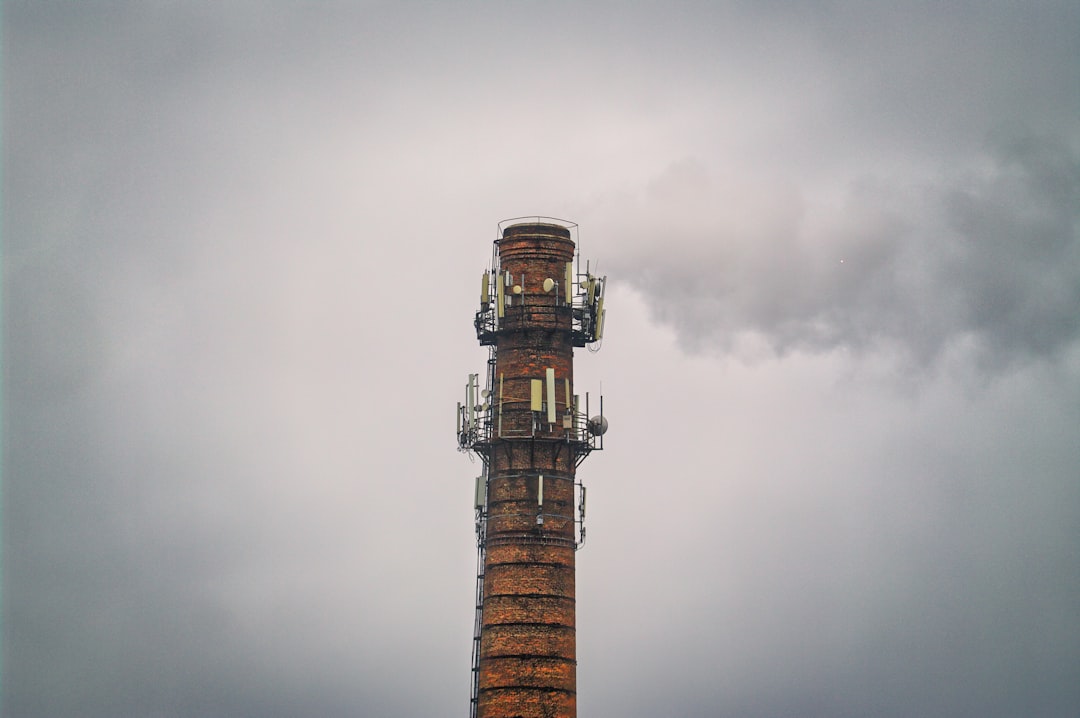brown and black tower under cloudy sky, Old red brick industrial smokestack with satellite dishes