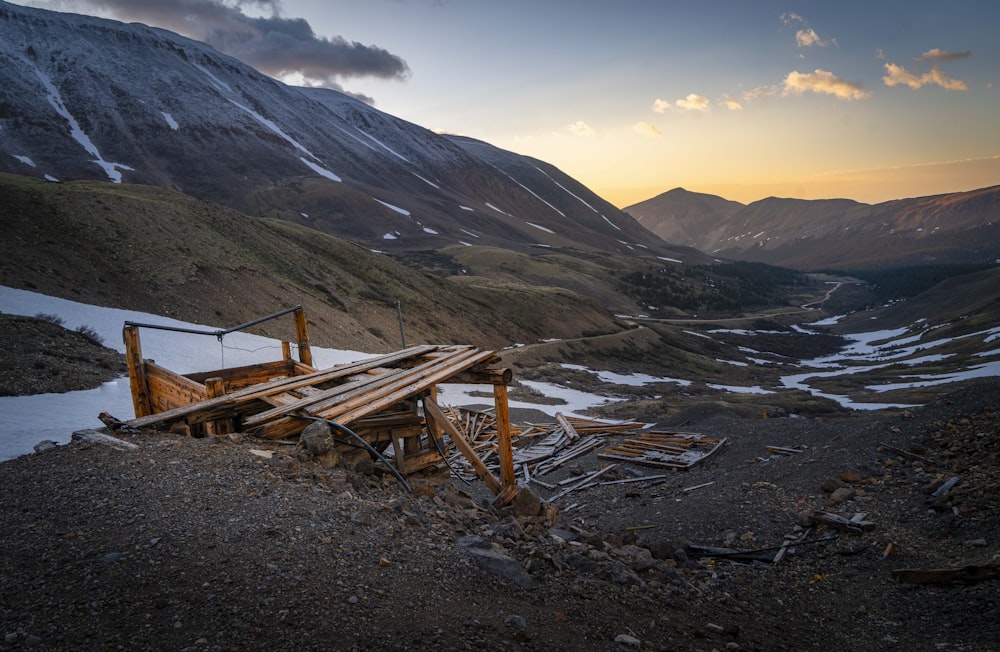 brown wooden bench on gray rocky ground near brown mountain under blue sky during daytime