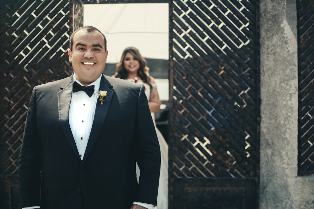 man in black suit standing near black brick wall