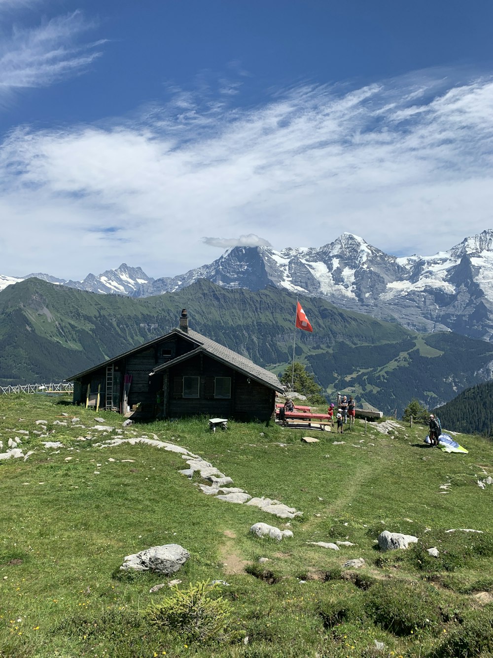 brown wooden house on green grass field near mountain under white clouds and blue sky during