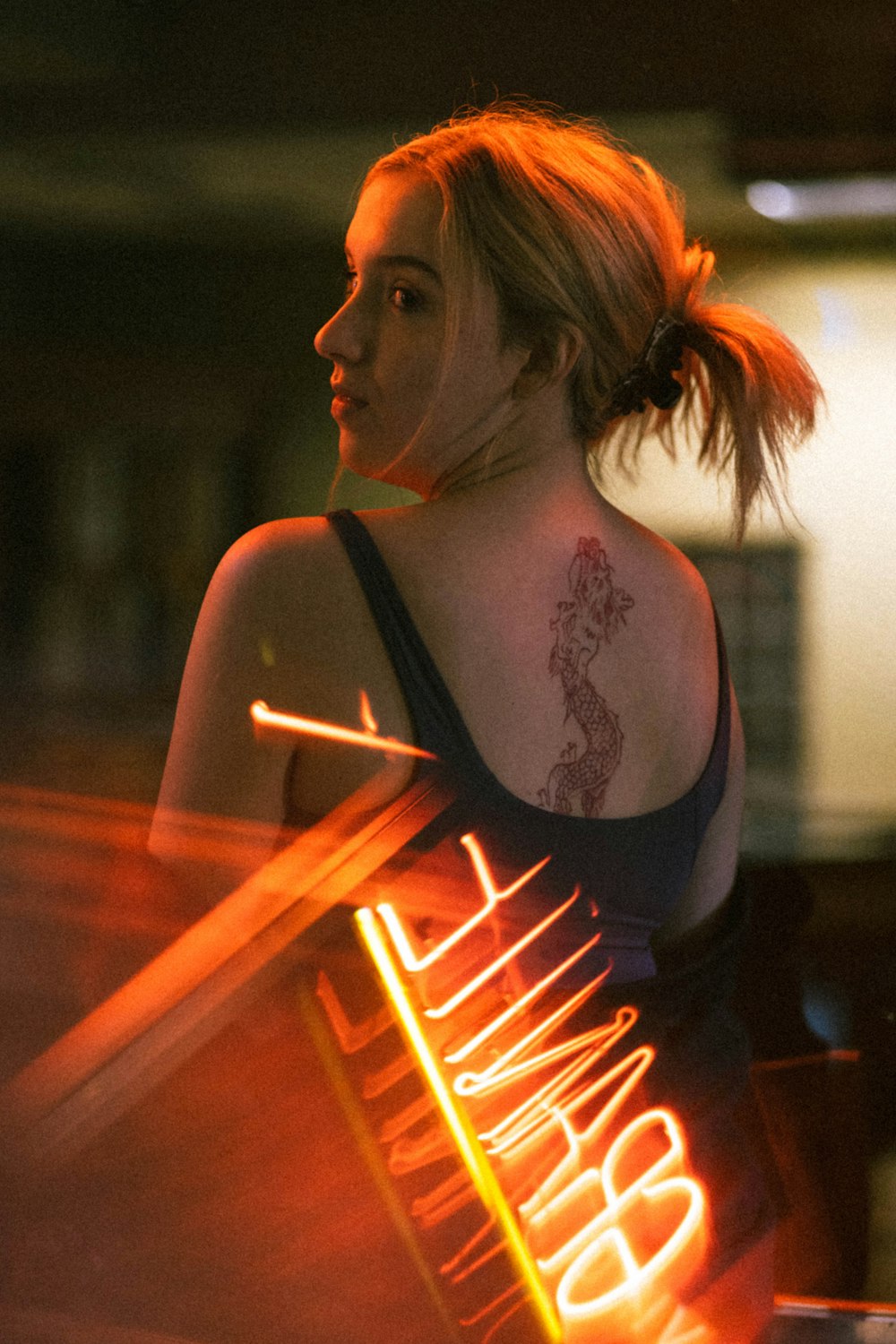 a woman with a tattoo on her back holding a neon sign