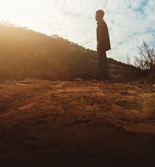 A person standing at a crossroads looking thoughtfully toward a bright horizon.