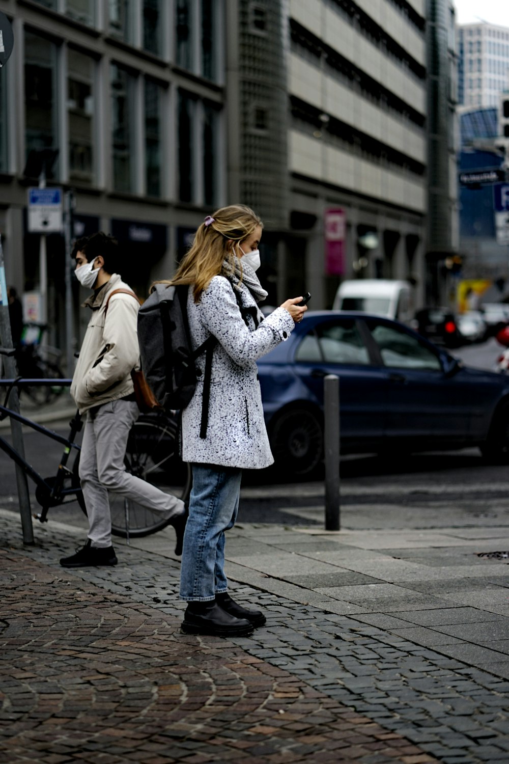 woman in gray coat standing on sidewalk during daytime