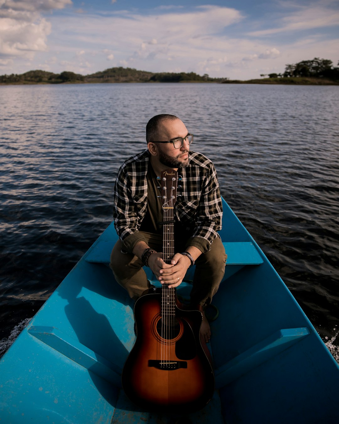 man in black and white long sleeve shirt playing acoustic guitar sitting on blue boat during