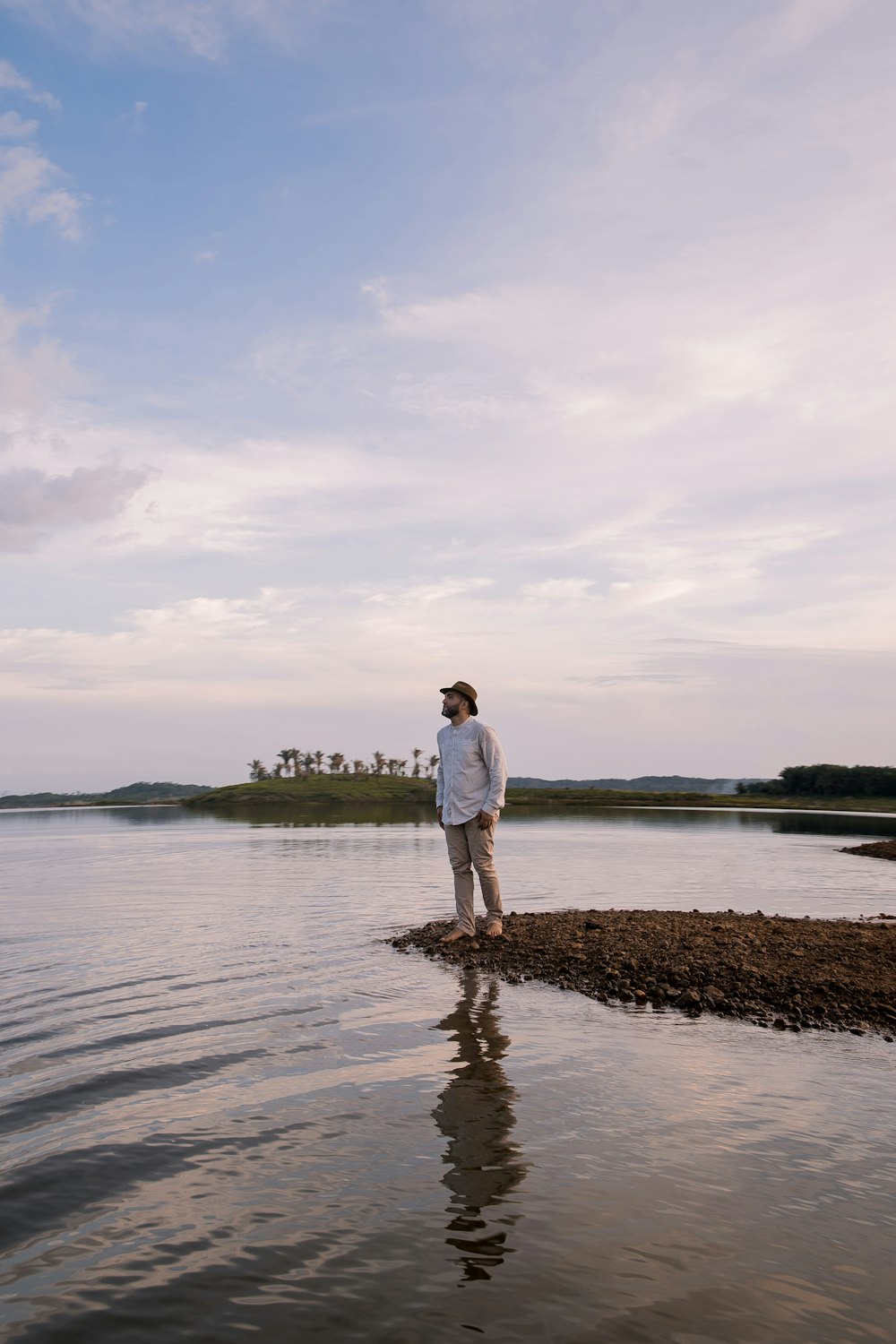 man in white shirt standing on brown rock near body of water during daytime