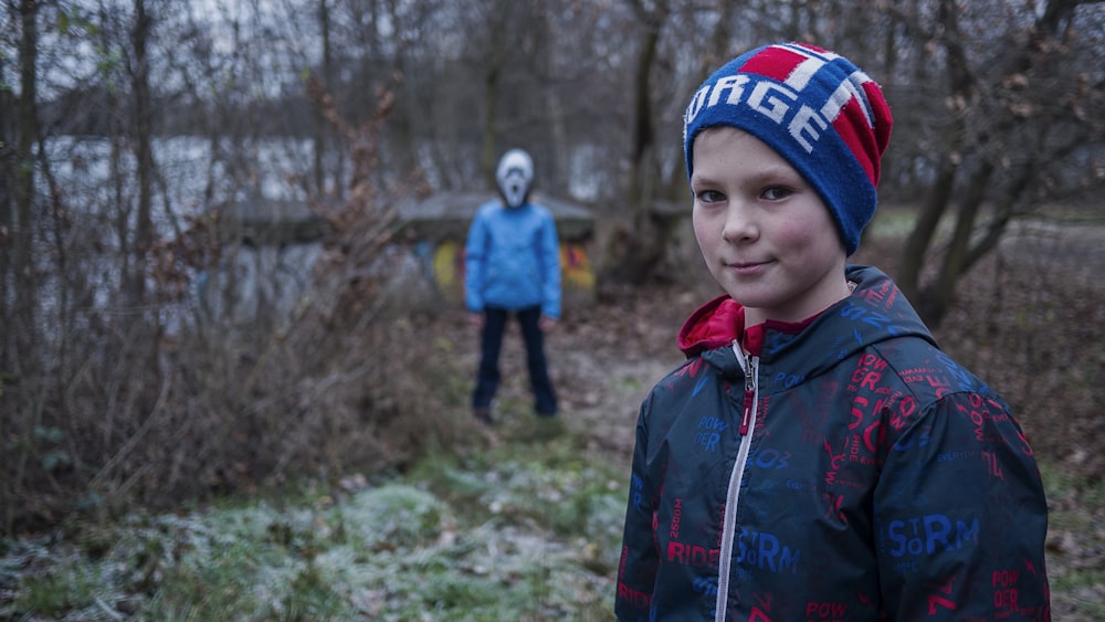 boy in red and black plaid jacket wearing blue and red knit cap