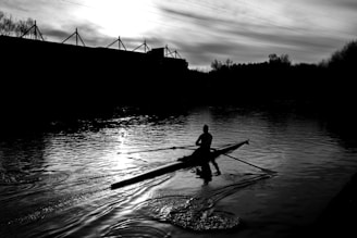 A serene view of a misty Thames riverbank with a lone rower gliding past ancient bridges.