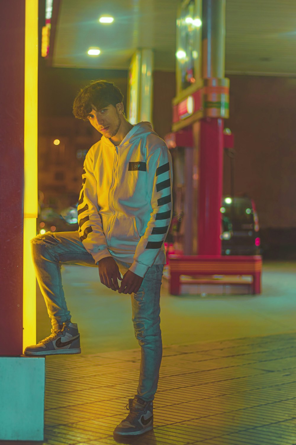 man in yellow blue and white adidas jacket and blue denim jeans standing on sidewalk during