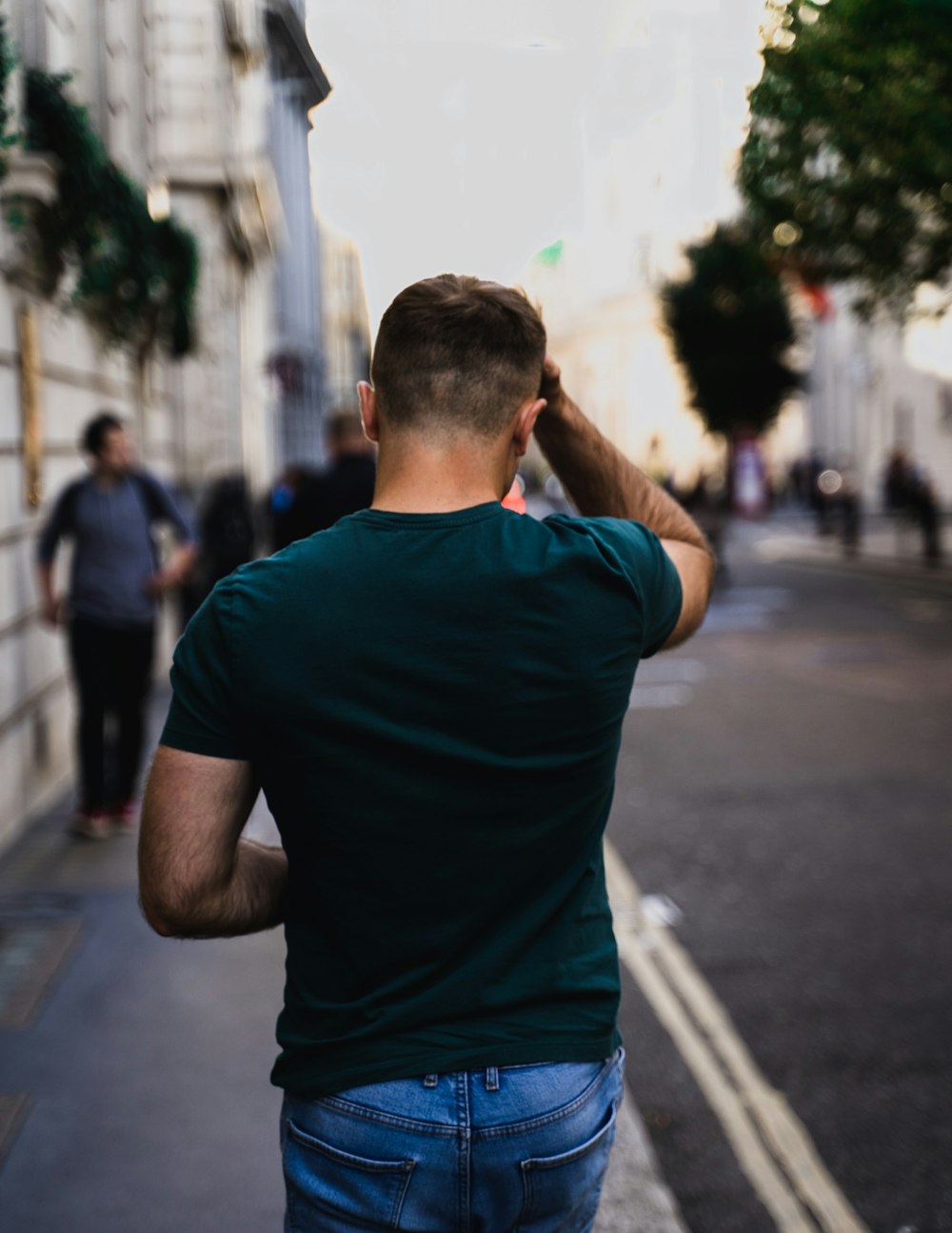 man in blue crew neck t-shirt standing on sidewalk during daytime