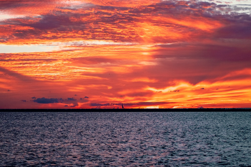 corpo d'acqua sotto il cielo nuvoloso arancione e grigio durante il tramonto