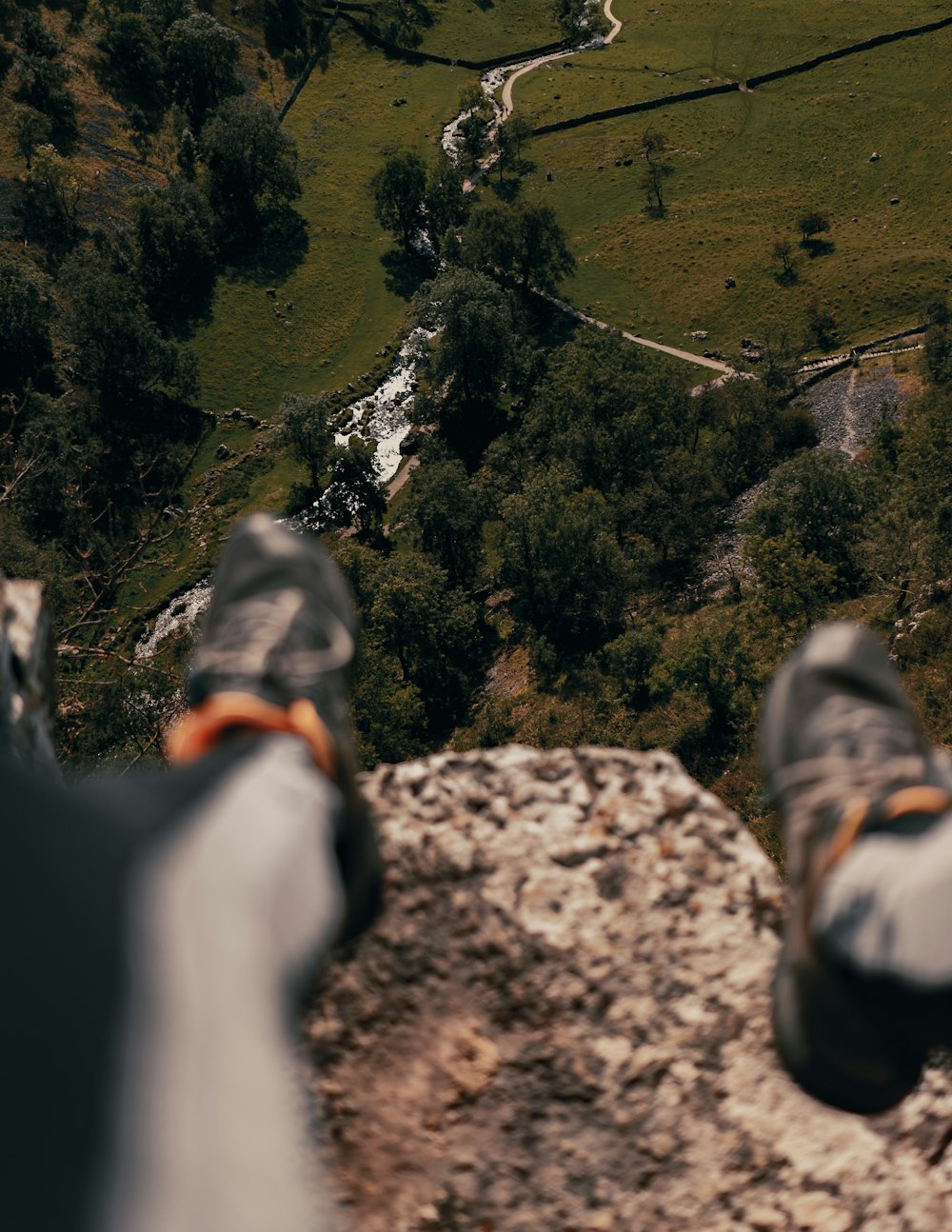 person in black pants and hiking shoes sitting on rock mountain during daytime