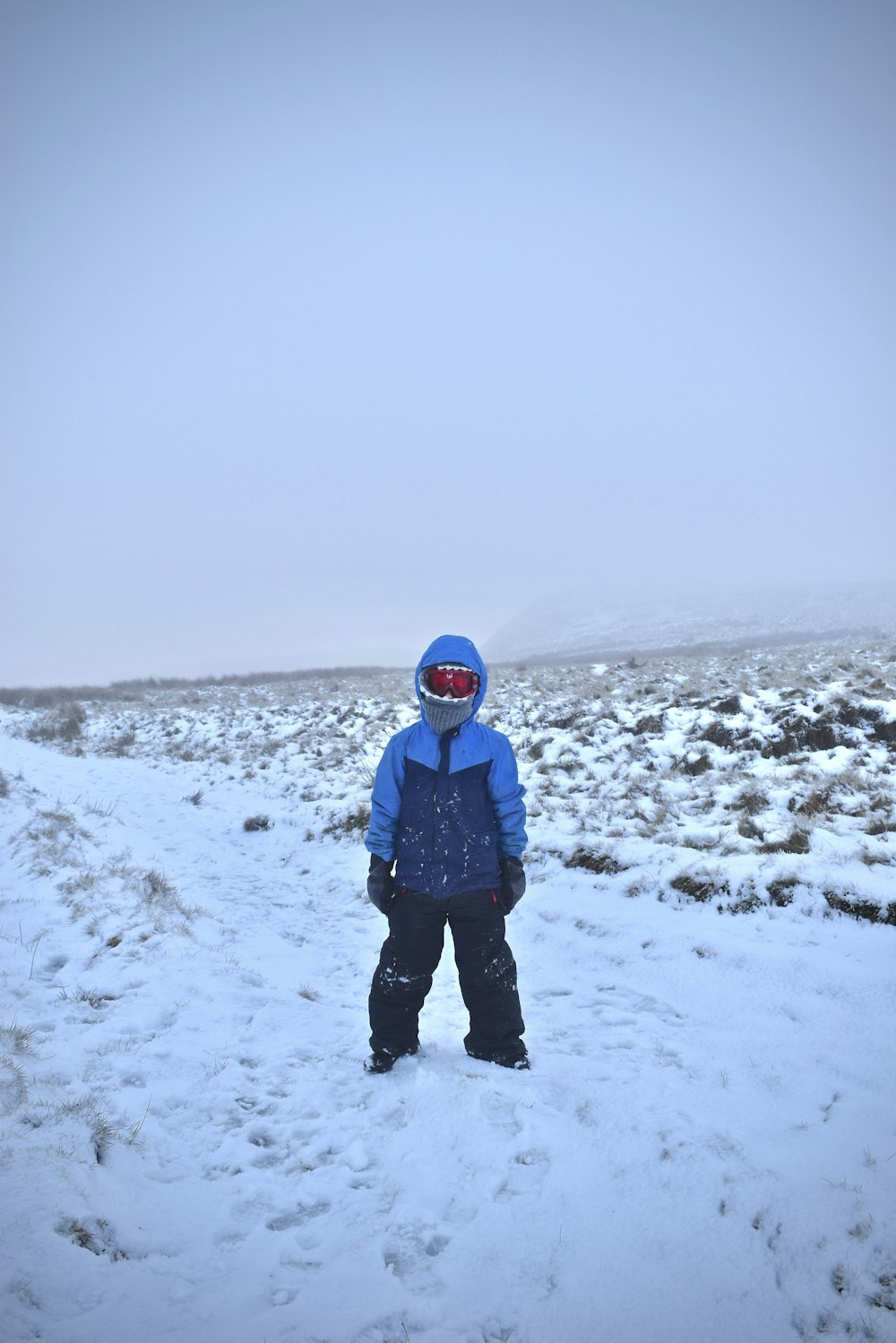 person in blue jacket and black pants standing on snow covered ground during daytime